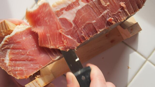 Spanish traditional pork jamon. A knife cuts a piece of hamon meat into thin slices in the kitchen, top view
