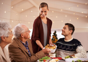 Family, dinner and smile at table on Christmas, together with food and celebration in home. Senior, mother and father with happiness at lunch with woman hosting holiday and dish of chicken on plate