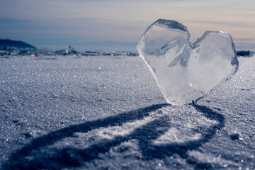 An icy heart in the sunset. An icicle in the shape of a heart on the ice of the lake. Frozen. Love of nature. Arctic landscape with a transparent icy heart, frozen snow. Selective focus.