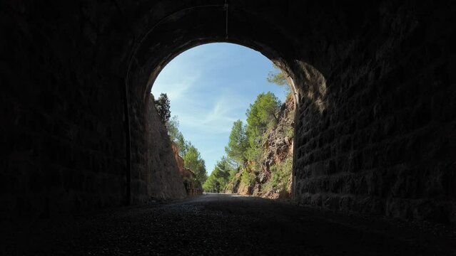 A man riding a mountain bike entering a dark tunnel, shot from inside. Via Verde Ojos Negros, Teruel, Spain.  4K 60FPS.