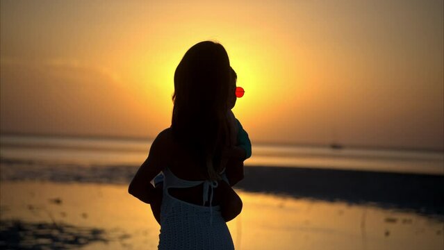 Slow motion of the silhouette of a latin woman and her son watching the sunset and then looking at the camera at a beach in Mexico