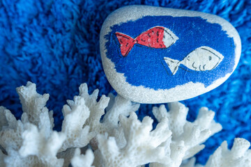 Two fish painted on a pebble swim past a coral.  Blue background