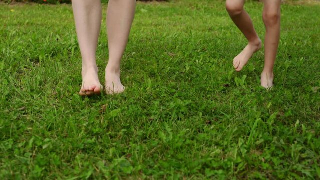 Mother and child walk barefoot on the grass on a lawn in a city park. Concept of a healthy lifestyle, hardening, prevention of flat feet