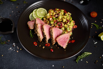Sliced Organic grilled Tuna fillet covered with sesame seeds and salsa on black ceramic plate