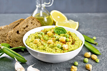 Hummus from green peas in bowl with bread on stone table