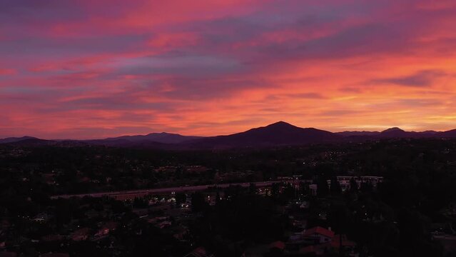 Drone panning shot over homes in Chula Vista and highway 54 during vibrant sunrise.