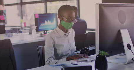 Image of financial data processing over businesswoman with face mask using computer in office