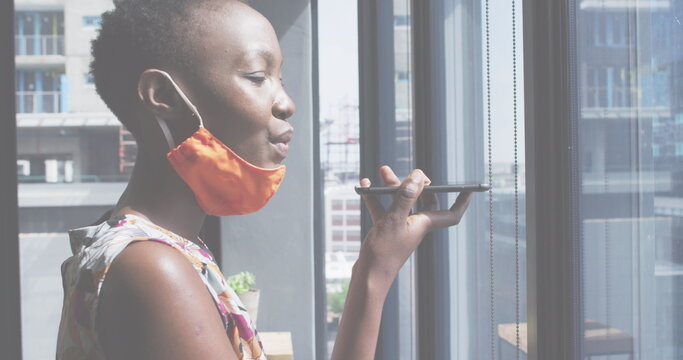 Image of financial data processing over businesswoman with face mask using smartphone in office