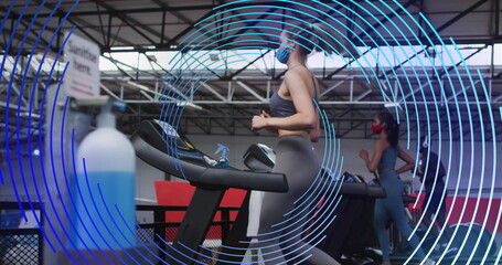 Image of blue spiral rotating over women in face masks exercising on running machines