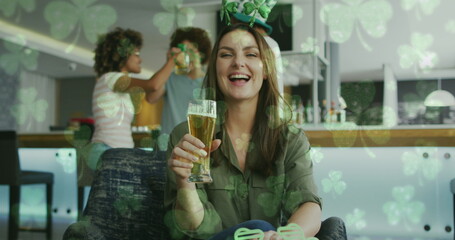 Image of clovers over happy diverse friends wearing clover shape items and drinking beer