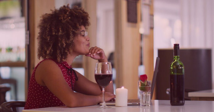 Image of heart icons over happy biracial woman with wine having laptop image call