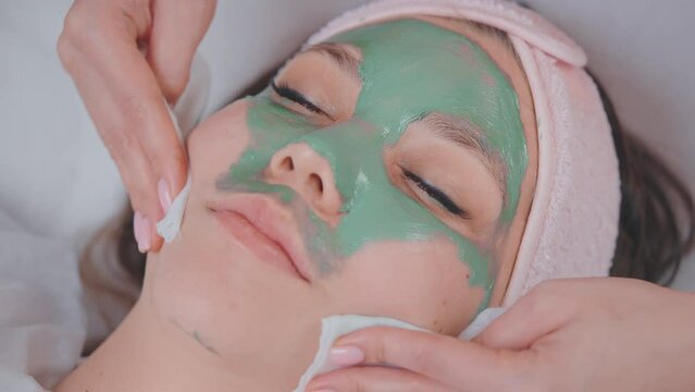Cosmetologist removes clue mask from woman's face uses wipes in beauty salon.