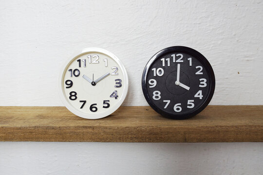 White and Black alram clock show time difference on wooden shelves