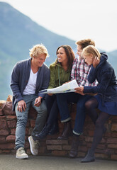 Happy people, friends and map for direction, location or planning next destination on stone wall. Young group looking or checking route, path or paper on holiday weekend or outdoor vacation in nature