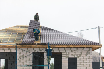 Fototapeta na wymiar Workers install tiles on the roof of a house in winter