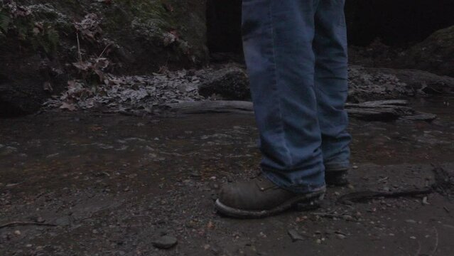 close up of a hikers boots as he approaches a stream where he reaches into his backpack to retrieve a tin cup to get water from the creek