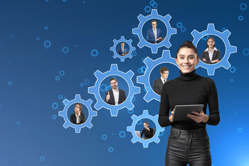 Smiling young businesswoman with tablet and creative cogwheels with happy european businesspeople inside on blue background. Teamwork and business mechanism system.