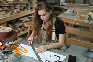 Fototapeta premium A young woman is training to be a carpenter in the workshop. She works with a laptop computer in a wood workshop. female carpenter contact customers by smartphone. SME orders, Start-ups and small