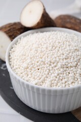 Tapioca pearls in bowl and cassava roots on table, closeup
