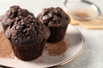 Delicious chocolate muffins and cacao powder on light grey table, closeup. Space for text