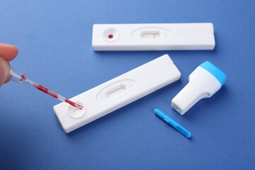 Woman dropping blood sample onto disposable express test cassette with pipette on blue background,...