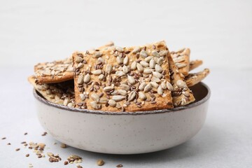 Cereal crackers with flax, sunflower and sesame seeds in bowl on light textured table, closeup