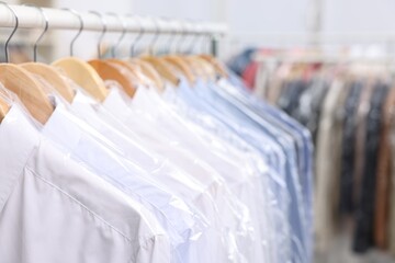 Dry-cleaning service. Many different clothes in plastic bags hanging on rack indoors, closeup