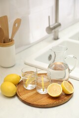 Fototapeta na wymiar Jug, glasses with clear water and lemons on white table in kitchen