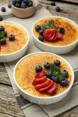 Delicious creme brulee with berries and mint in bowls on wooden table