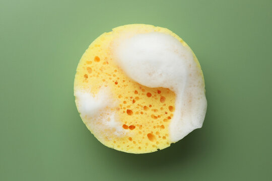 Yellow sponge with foam on green background, top view