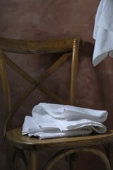 White terry towels on wooden chair against brown background