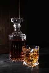 Whiskey with ice cubes in glass and bottle on black wooden table
