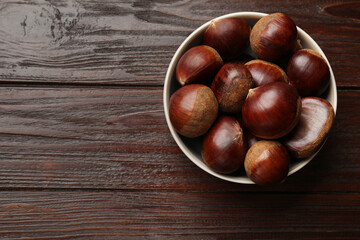Sweet fresh edible chestnuts in bowl on wooden table, top view. Space for text