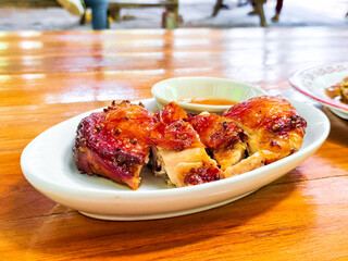 Thai style grilled chicken with herb on white dish on wooden table. Delicious food concept.