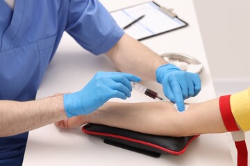 Doctor taking blood sample from patient with syringe at white table in hospital, closeup