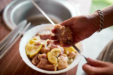 A person prepares marinated kebabs on skewers for a summer barbecue at a home backyard, captured in close-up detail.