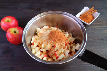 Ground cinnamon and unrefined sugar added into the pot of diced apples for making apple compote