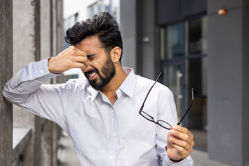 A male professional in distress pinching the bridge of his nose, signifying headache or stress,...