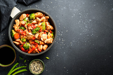 Stir fry chicken and vegetables and sesame at black background. Asian cuisine. Top view with space for design.