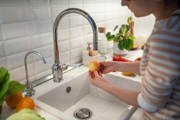 Female thoroughly washing fresh yellow apple in tap water to clean from food wax covering....