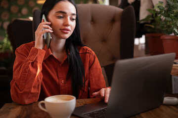 Serious young web store owner calling to client to confirm ordering of purchase, content managers monitoring work of site while sitting in cafe uses laptop computer