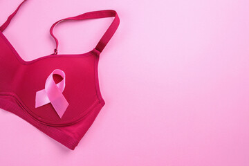 Pink ribbon attached to brassiere on pink background with empty space