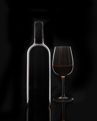 Isolated bottle of red wine and red glass of wine on black background without label