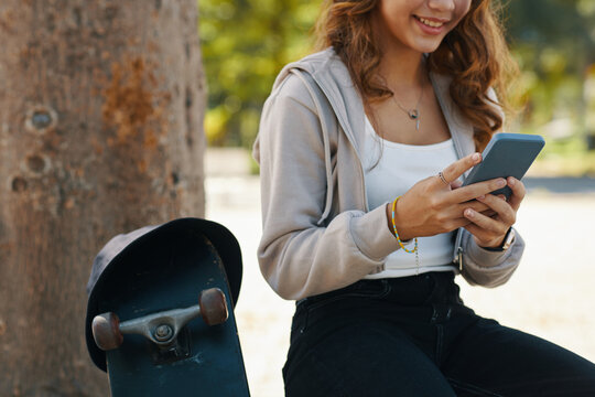 Smiling teenage girl sitting on bench in park and texting friend