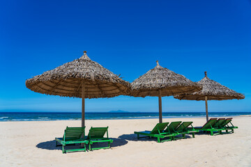 Sun loungers on the tropical sand beach near sea water in sun weather without people in Da Nang, Vietnam