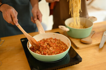 Closeup young couple cooking bolognese spaghetti sauce for dinner in a frying pan