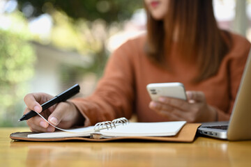 Young woman looking through window, holding pen and making notes