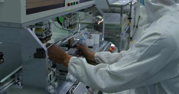 An operator in a protective gown works on an assembly line for the production of electronic devices.