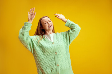 Portrait of young positive woman dancing raised hands up of joy and happiness against yellow studio...