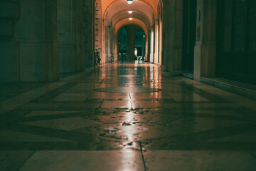 Fototapeta premium Under the porticoes of a historic building in the city center at night. Old building in the city center with lights. Reflecting stone floor. Udine city center old bulding in the night. Historical city